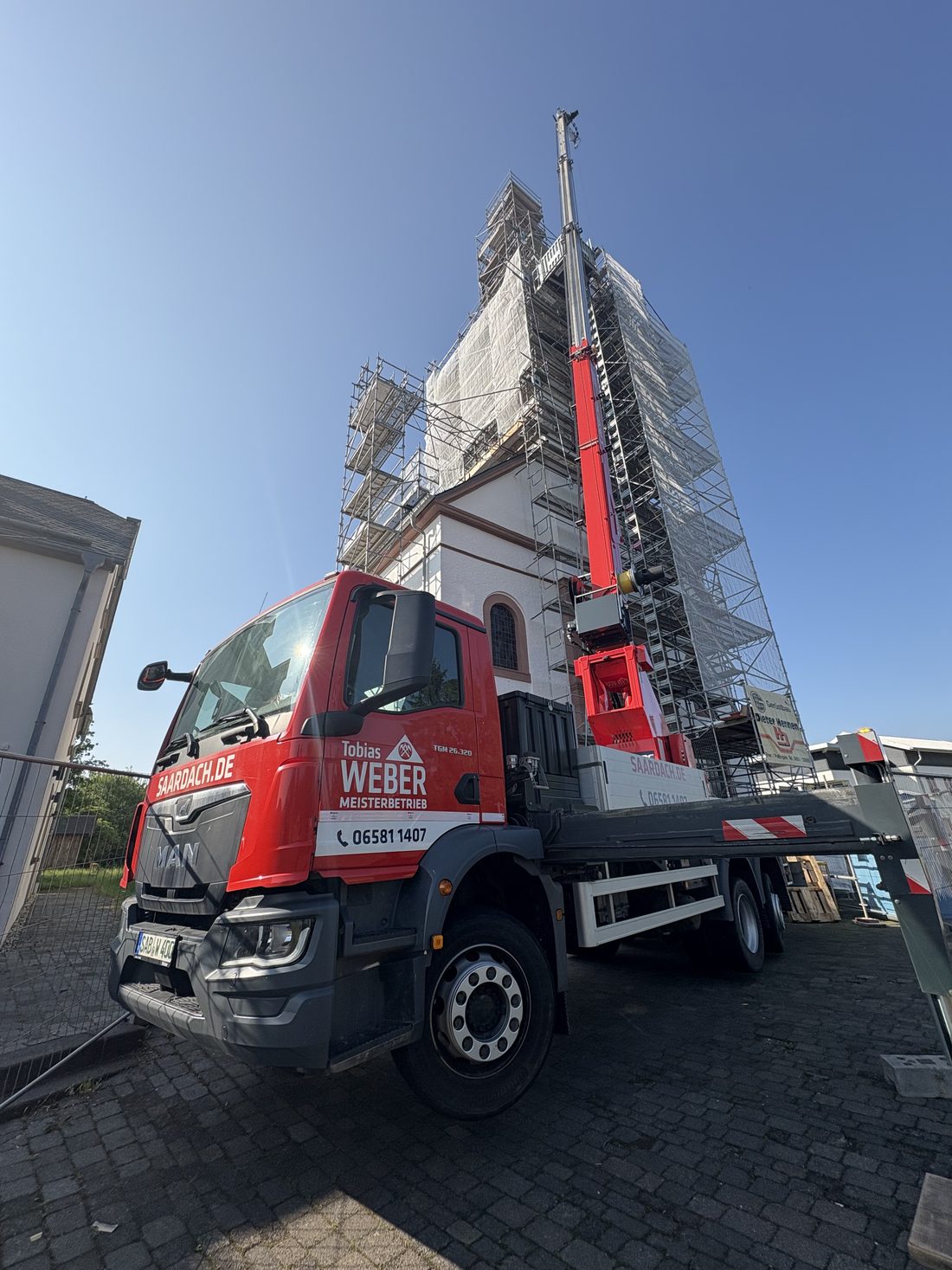 Lkw mit Ladekran der Dachdeckerei Weber vor einem eingerüsteten Kirchturm